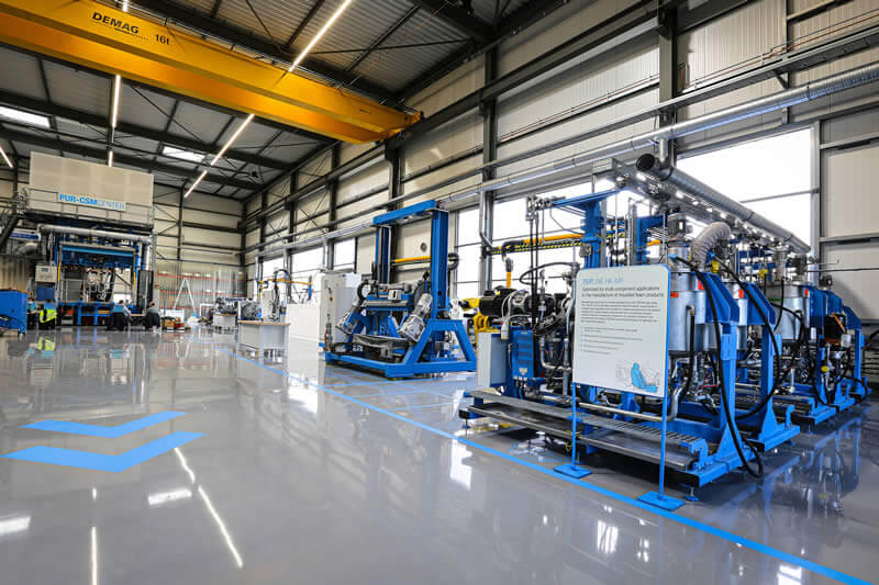 Better utilization and shorter distances within the approximately 1000 square meter hall. In the foreground: 6-component high-pressure metering machine with 40 ton mold carrier.